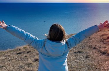 The girl stands facing the sea with her arms outstretched to the sun, March 2023